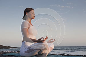 Young woman meditation in a yoga pose at the beach on sunset