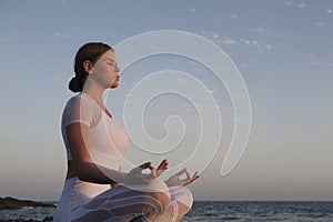 Young woman meditation in a yoga pose at the beach on sunset