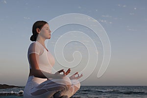 Young woman meditation in a yoga pose at the beach on sunset