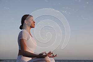 Young woman meditation in a yoga pose at the beach on sunset