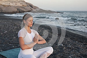 Young woman meditation in a yoga pose at the beach on sunset. Breathing practise