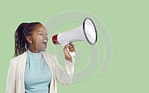 Young woman with megaphone in her hand shouting advertising something on light green background.