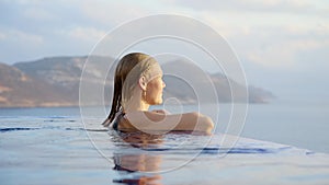 young woman at midday in infinity pool on edge of abyss. girl looks into distance, concept of loneliness and happiness