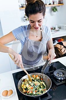 Young woman mixing chards, potatoes, red pepper and eggs into the pan.