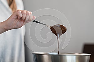 Young woman mixing chocolate in steel bowl to make candys