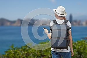 Young woman with mobile phone in hands and portable solar battery on background of river outdoors.
