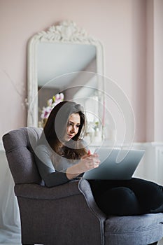 Young woman in modern luxury apartment, sitting comfortable in armchair holding computer on her laps, relaxing, working