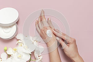 Young woman moisturizes her hand with cosmetic cream lotion opened container with cream body milk White Phalaenopsis orchid