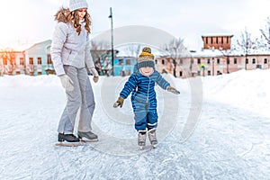 Young woman mom skates with her young son, a boy of 3-5 years. In the winter in the city on the rink. The first lesson