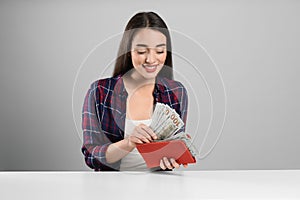 Young woman with money and wallet at table on light grey background