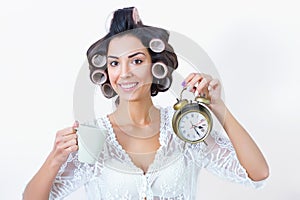 Young woman morning rush with coffee, clock and hair curlers