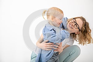 Young woman mother holding catching looking at lovely little blond girl baby daughter wearing oversized denim shirt.
