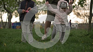 Young woman mother learn to walk little baby daughter girl walking on grass in spring park. Happy infant child take