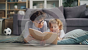 Young woman mother reading book to child lying on floor on blanket together