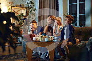 Young woman, mother spending time with her children, boys and little girl, family sitting on couch at home in evening