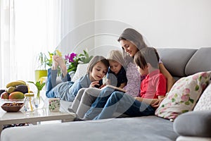 Young woman, mother with three kids, reading a book at home, hugging and laughing