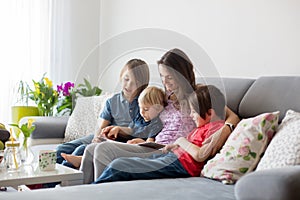 Young woman, mother with three kids, reading a book at home, hugging and laughing