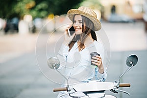 Young woman on motorcycle talking on the phone and drink coffee on the street