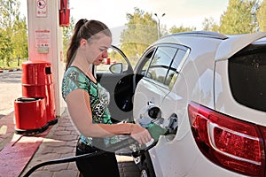 Young woman-motorist fills her car with benzine at gas station