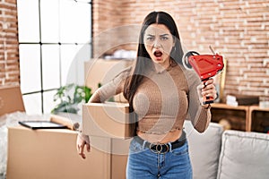 Young woman moving to a new home packing boxes in shock face, looking skeptical and sarcastic, surprised with open mouth