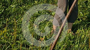 Young woman mowing the green grass with the scythe on the summer field by the river. Beautiful landscape. Work in the