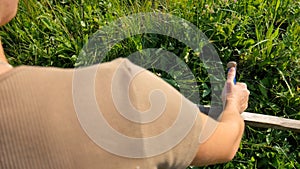 Young woman mowing the green grass with the scythe on the summer field by the river. Beautiful landscape. Work in the