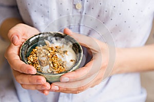 Young woman with muesli bowl. Breakfast cereals with nuts, pumpkin seeds, oats and Yogurt in bowl. Hands holding granola