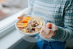 Young woman with muesli bowl, girl eating breakfast cereals nuts, pumpkin, oats and apple in bowl.