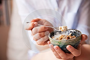 Young woman with muesli bowl. Girl eating breakfast cereals with nuts, pumpkin seeds, oats and yogurt in bowl