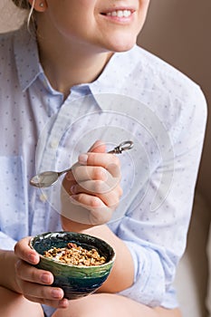 Young woman with muesli bowl. Girl eating breakfast cereals with nuts, pumpkin seeds, oats and yogurt in bowl