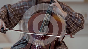 Young woman musician with bow in hands playing cello at home