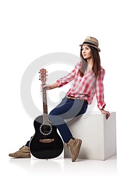 Young woman musician with guitar sitting on cube