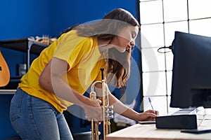 Young woman musician holding trumpet writing on notebook at music studio