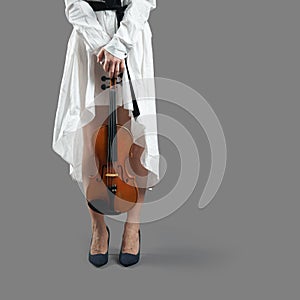 Young woman musician holding a violin in her lowered hands at her feet isolated on gray