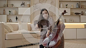 Young woman musician with long hair tuning cello sitting at home