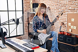 Young woman musician playing electric guitar at music studio