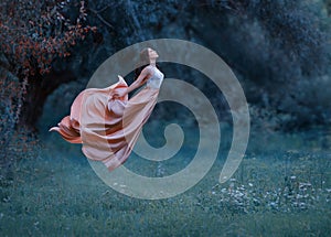 A young woman, a mysterious witch is floating in the air like a butterfly. A luxurious, long dress flutters in the wind