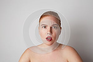 Young woman with naked shoulders and emotional face looking at the camera and posing on the gray wall. .