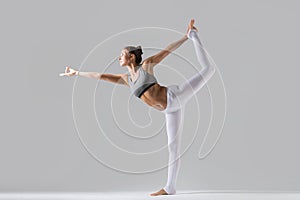 Young woman in Natarajasana pose, grey studio background