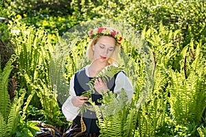 Young woman in national clothes and wreath against the background of a green fern. Ligo Latvian holiday