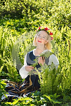 Young woman in national clothes and wreath against the background of a green fern. Ligo Latvian holiday