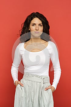 Young woman with natural makeup and long curly black hair wearing while clothes over red studio wall