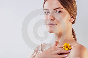 Young woman with natural makeup and smooth skin holding a flower. Organic cosmetics concept