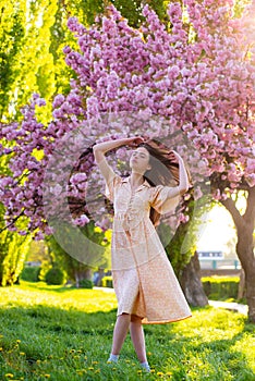 Young woman near blossom park. Spring girl. Woman on spring blooming tree. Beautiful young woman in summer style outfit