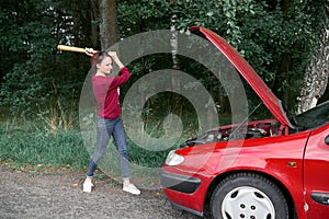 A young woman is near a broken car, has stress and rage, wants to smash her car with a baseball bat