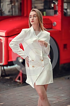 Young woman near english bus. London red bus - girl enjoying life. portrait of Beautiful femail model wearing at white long jaket