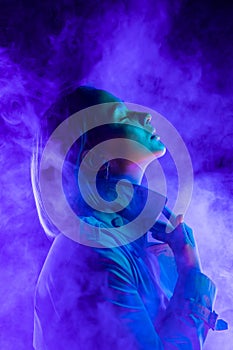 Young woman in neon multi-colors light on smoke, steaming background. stylish