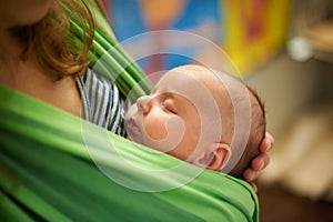 Young woman with newborn infant baby in a sling with a blurred background at home