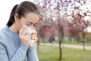 Young woman with nose wiper near blooming tree. Allergy concept