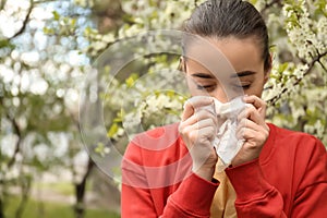 Young woman with nose wiper near blooming tree. Allergy concept